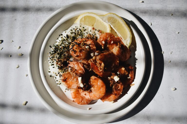 garlic shrimp, rice with furikake, and lemon slices on a smaller plate that is stacked onto a bigger plate