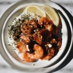 garlic shrimp, rice with furikake, and lemon slices on a smaller plate that is stacked onto a bigger plate.