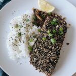 furikake salmon on a white plate with rice, and mixed mushrooms, topped with green onion, lemon, and more furikake.
