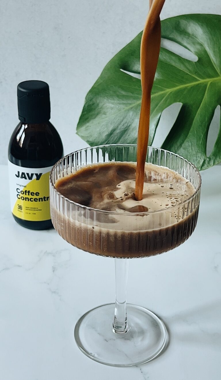 espresso martini being poured in a coup glass with coffee concentrate in the background