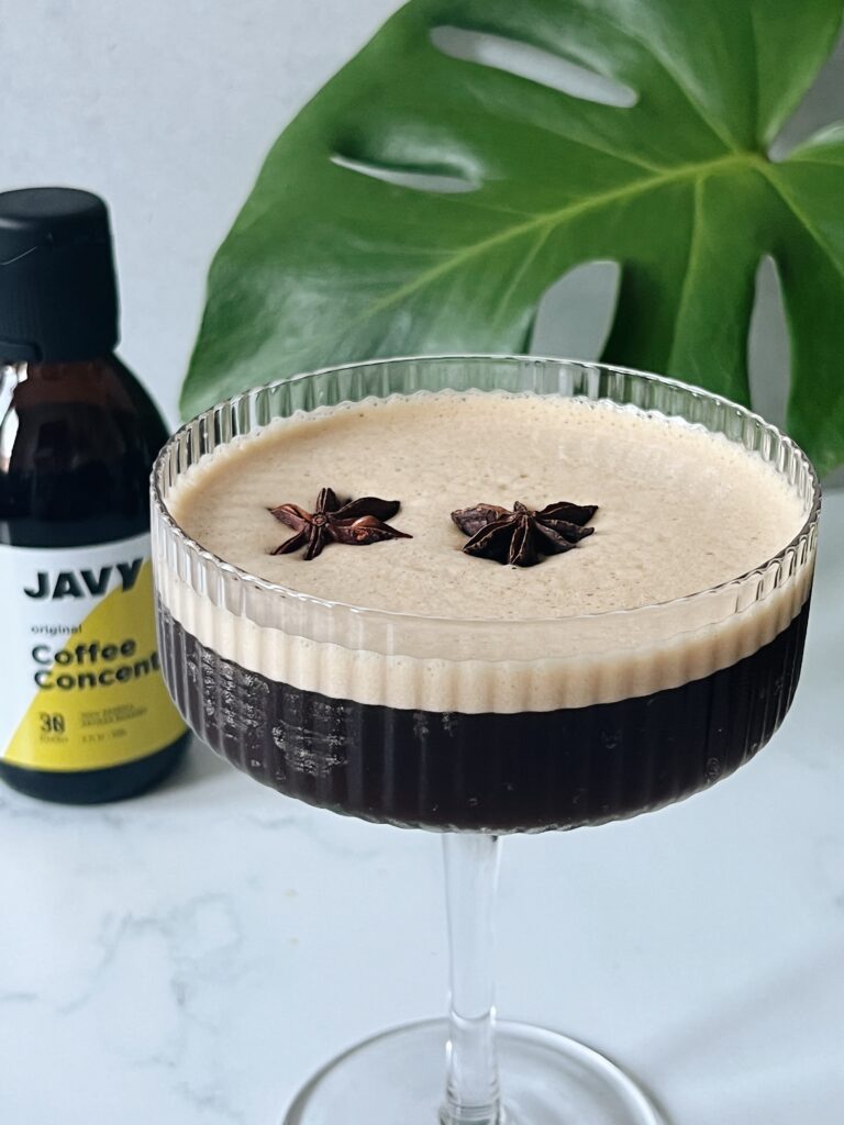 espresso martini topped with star anise in a coupe glass with coffee concentrate and a monstera leaf in the background