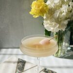 Lychee martini sitting on top of stone board with flowers in the background